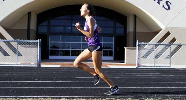 Fletcher High distance runner Kayley DeLay passes the Senators’ field house as she strides to victory in the 3,200 meters during Fletcher’s lone home track meet in March. DeLay won a gold and a silver medal during the state championship meet at IMG Academy in Bradenton. (photo by Rob DeAngelo)