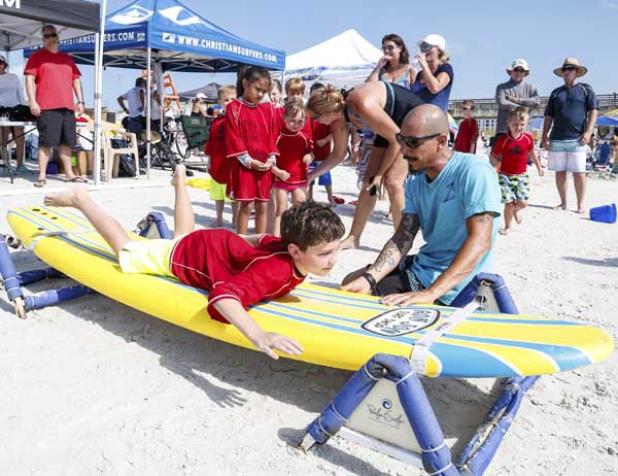 Surfing instructor Felix Santiago gives a young surfer a lesson on how to paddle prior to taking the grom out into the water. (photo by David Rosenblum)