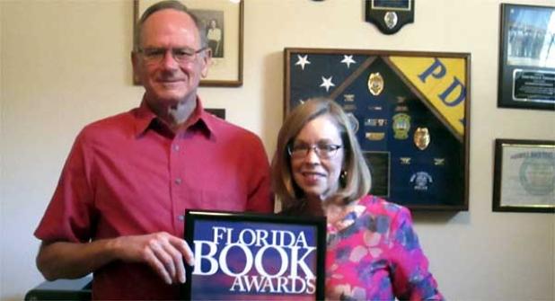 Bruce and Jackie Thomason show his 2016 Florida Book Award for “Perception of Power.” Mementoes of Bruce Thomason's 45-year law enforcement career hang on the wall behind them in their Jacksonville Beach home. (photo by Eleanor Snite)