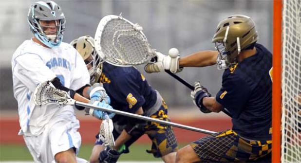 Sharks attacker Ben Buchanan (in white) fires the ball past St. Thomas Aquinas goalie Michael Adler as he scores in last Saturday’s boys lacrosse state championship game at Jupiter Community High School. Buchanan had two goals but the previously unbeaten Sharks fell to the Raiders 13-11. (photo by Rob DeAngelo)