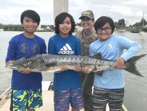 Alton and Jayden Azcona, along with Aiden Paul Florin, were so excited about their barracuda catch, they just had to show it to FWC Officer Miano at the dock. (photo courtesy of FWC)